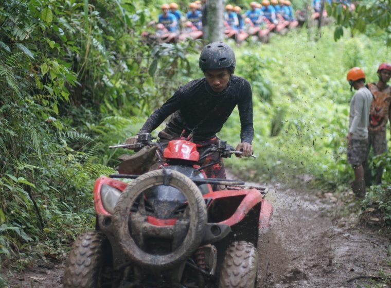 Rider on a red ATV splashing through jungle mud