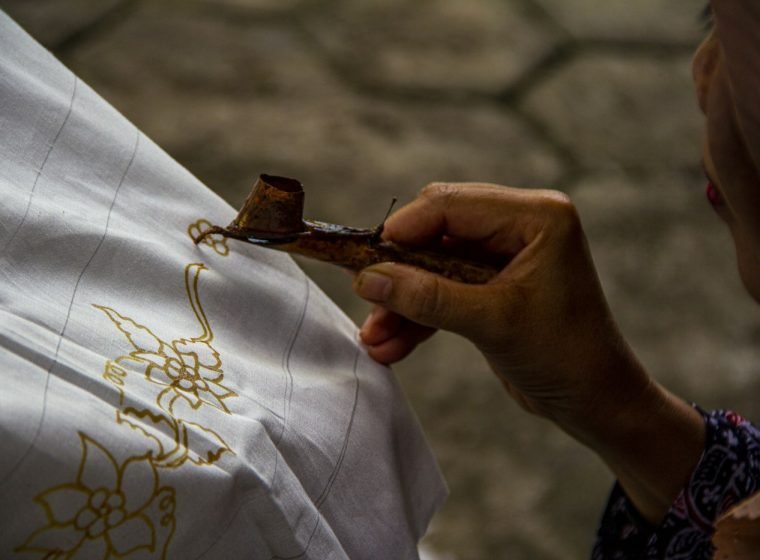 Artist drawing hot wax onto fabric with a canting tool