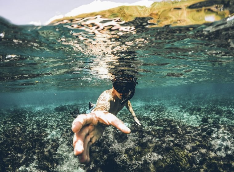 Snorkeler reaching towards the camera over a coral reef