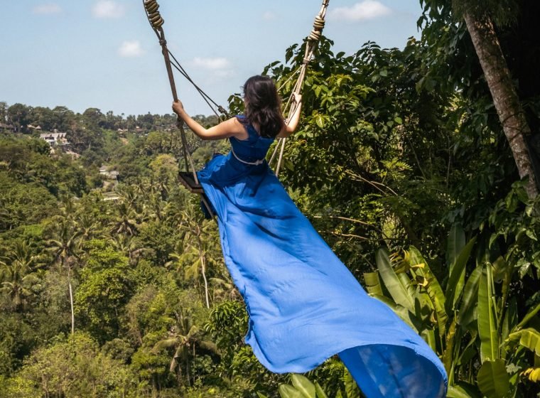 Woman in a blue dress on a giant swing over the jungle